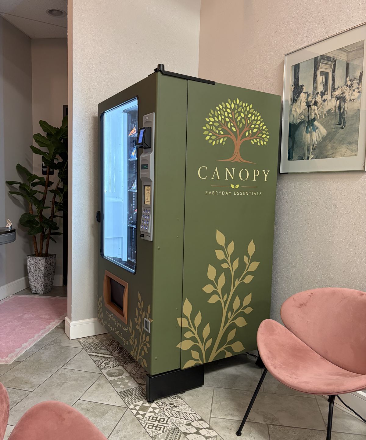 A Canopy machine wrapped in olive green with a gold vine, installed in a studio lobby