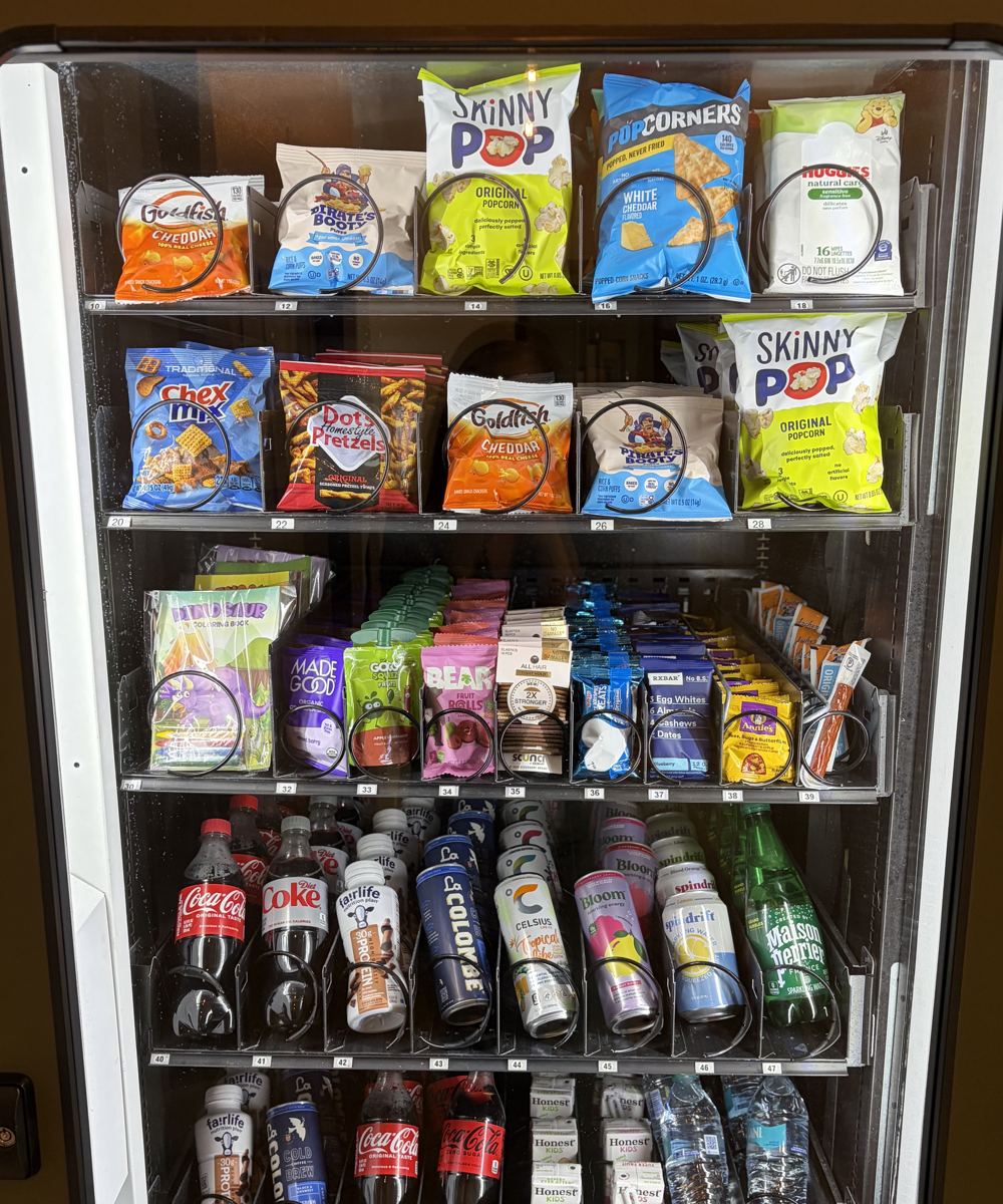 The shelves of a stocked Canopy machine: SkinnyPop, Popcorners, Goldfish, MadeGood bars, Celsius, Bloom, Spindrift, and cold water